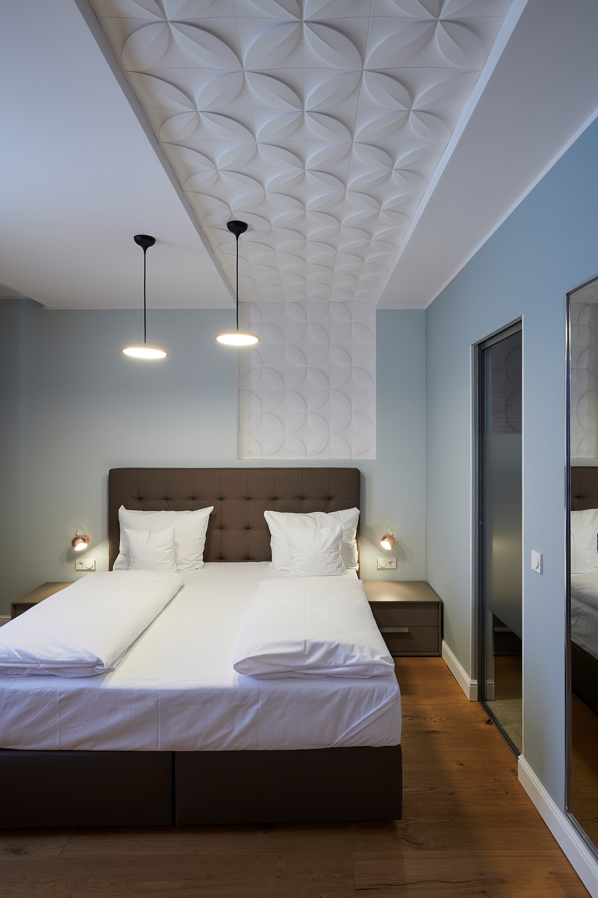 Panneaux muraux décoratifs posés au plafond, créant un effet texturé au-dessus du lit.